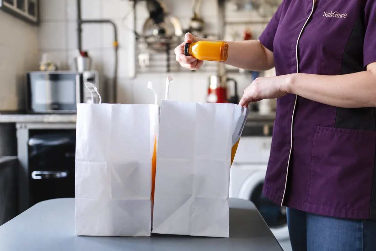 A person in a purple uniform unpacking groceries in a kitchen